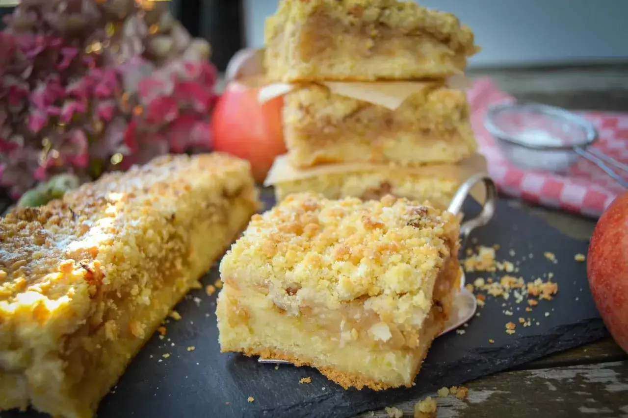Saftiger Apfelmuskuchen vom Blech mit Streuseln, wie von Oma gebacken. Ein St&uuml;ck davon liegt auf einer Kuchenschaufel.