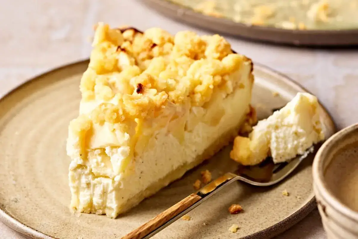 Ein St&uuml;ck Apfelkuchen mit Quark und Streuseln auf einem Teller, daneben eine Gabel mit einem St&uuml;ck Kuchen.