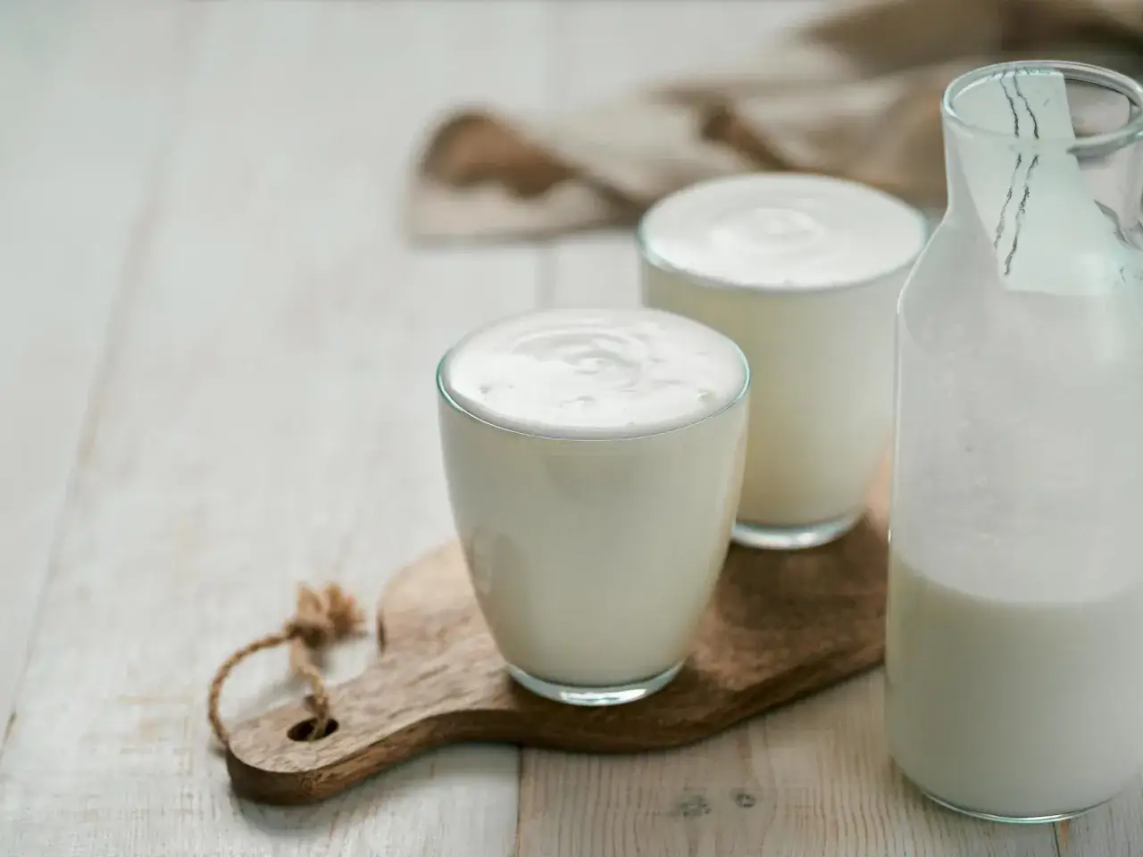 Erfrischender Ayran, perfekt zum selber machen. Zwei Gläser und eine Flasche gefüllt mit dem cremigen Getränk auf einem Holzbrett.