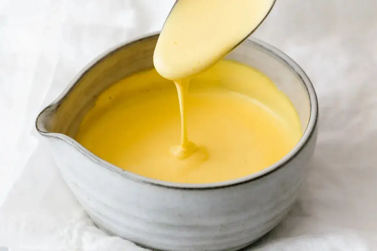 Cremige Sauce Hollandaise wird mit einem L&ouml;ffel in eine Sch&uuml;ssel gegossen. Perfekt, um Gerichte zu verfeinern.