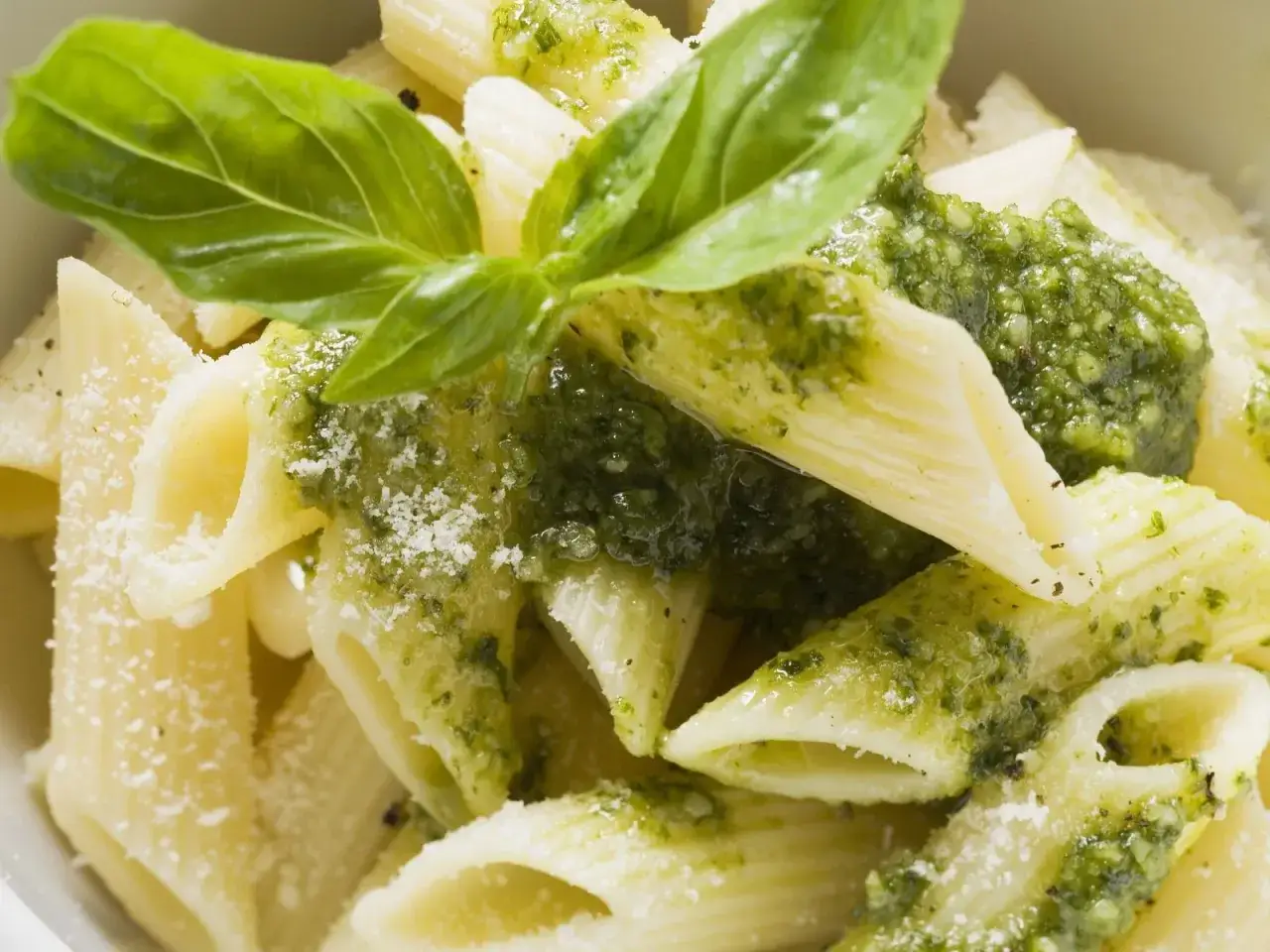 Penne-Nudeln mit frischem Basilikum Pesto und Parmesan bestreut. Ein Hauch von Sommer auf dem Teller.