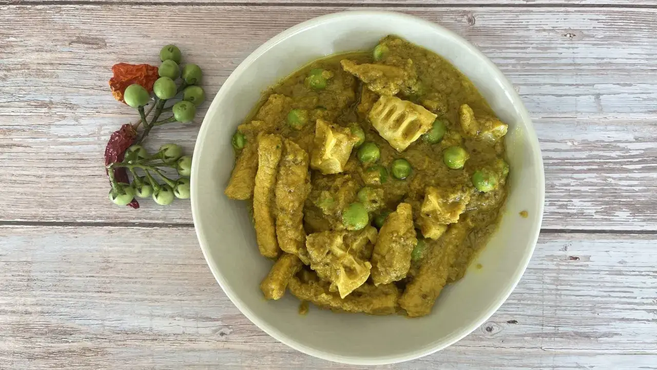 Sch&uuml;ssel mit gelbem, cremigem thai curry ohne kokosmilch, Erbsen und Lotuswurzel. Daneben ein Zweig mit gr&uuml;nen Beeren und getrockneten Chilis.