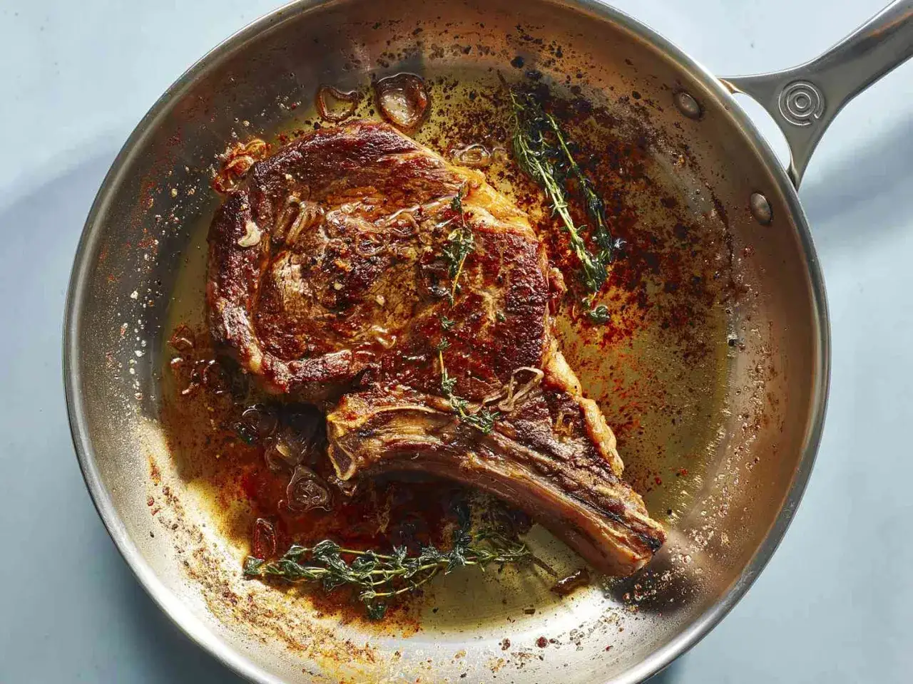 Ein saftiges Rib-Eye-Steak braten in einer Pfanne mit Kräutern und Zwiebeln.
