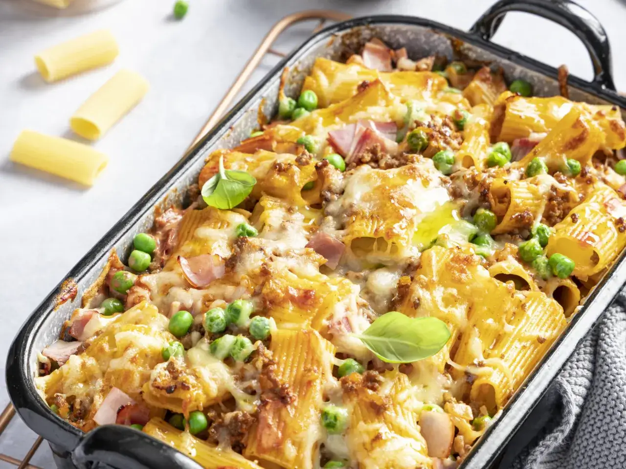 Herzhaftes Rigatoni al Forno mit Hackfleisch, Erbsen und geschmolzenem K&auml;se, garniert mit frischem Basilikum.