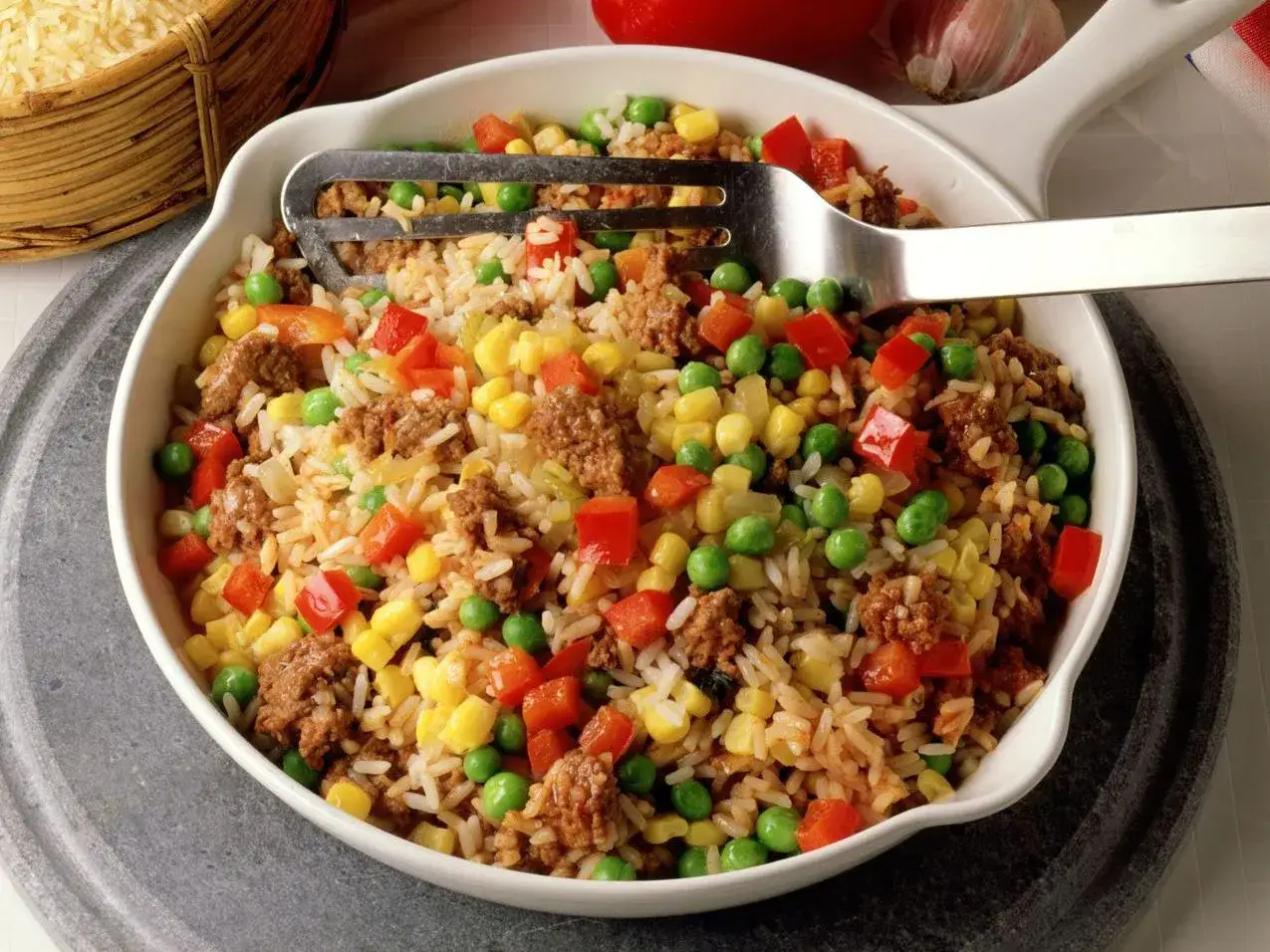 Reis mit Hackfleisch, Erbsen, Mais und Paprika in einer Sch&uuml;ssel, serviert mit einer Gabel.