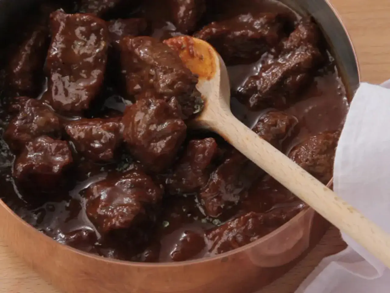 Ein dampfender Topf mit zartem Rindergulasch nach Omas Rezept, serviert mit einem Holzl&ouml;ffel.