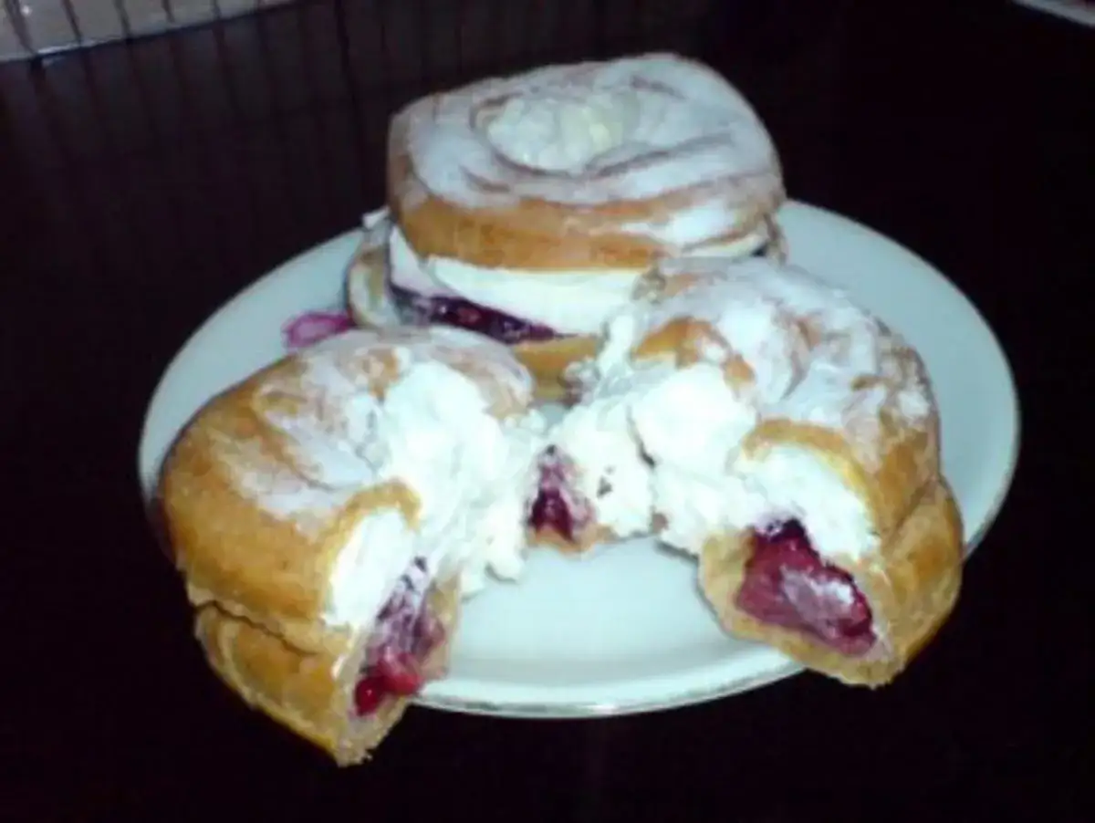 Zwei Windbeutel mit Kirschen und Sahne, bestäubt mit Puderzucker, auf einem Teller.