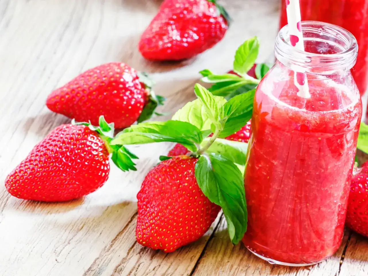 Erfrischender Erdbeer-Limetten-Smoothie in einer Glasflasche, umgeben von frischen Erdbeeren und Minze auf Holzhintergrund.