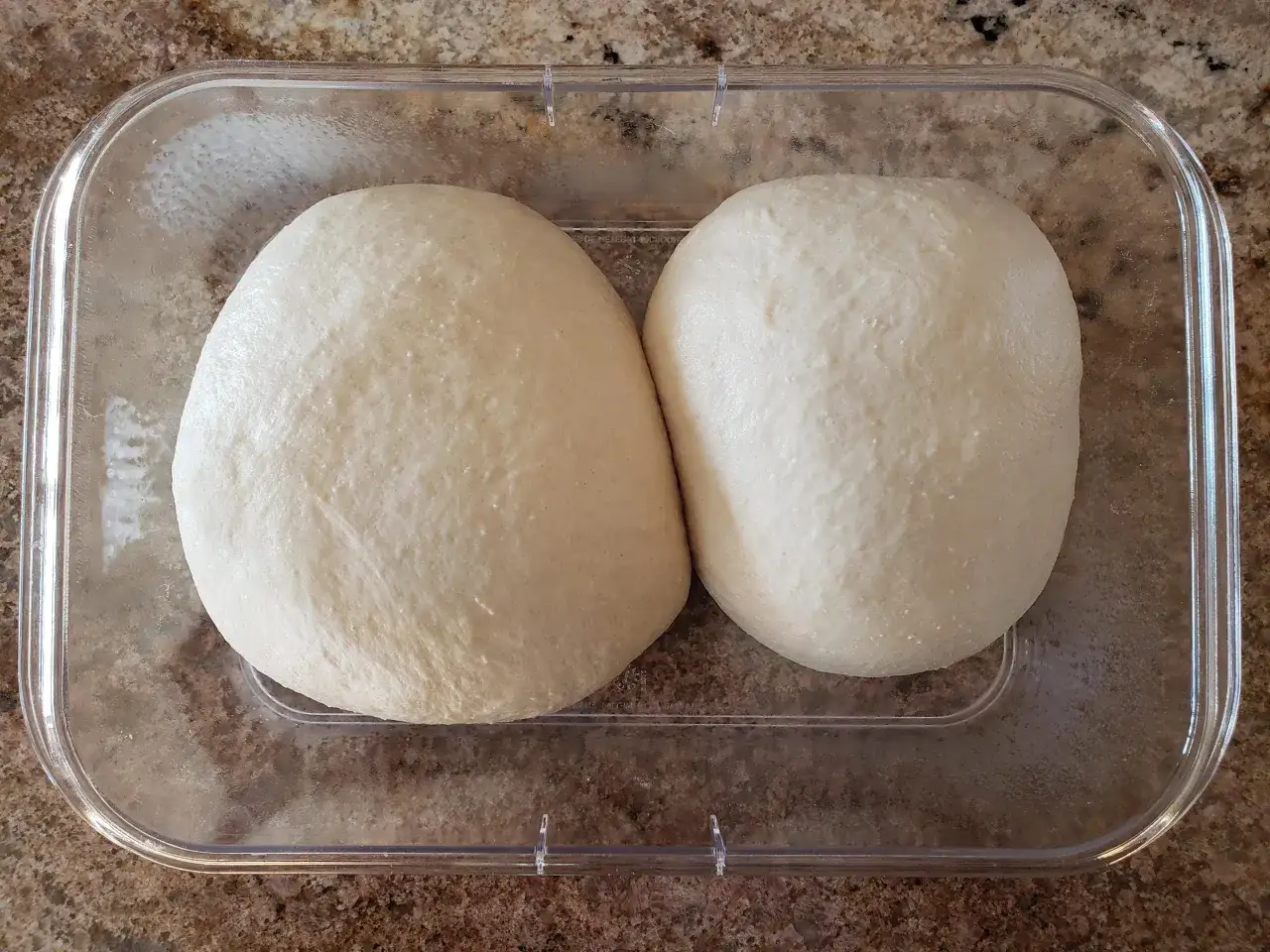 Zwei Teigkugeln ruhen in einer Plastiksch&uuml;ssel. Die Frage ist: wie lange muss ein pizzateig ruhen, damit er perfekt wird?