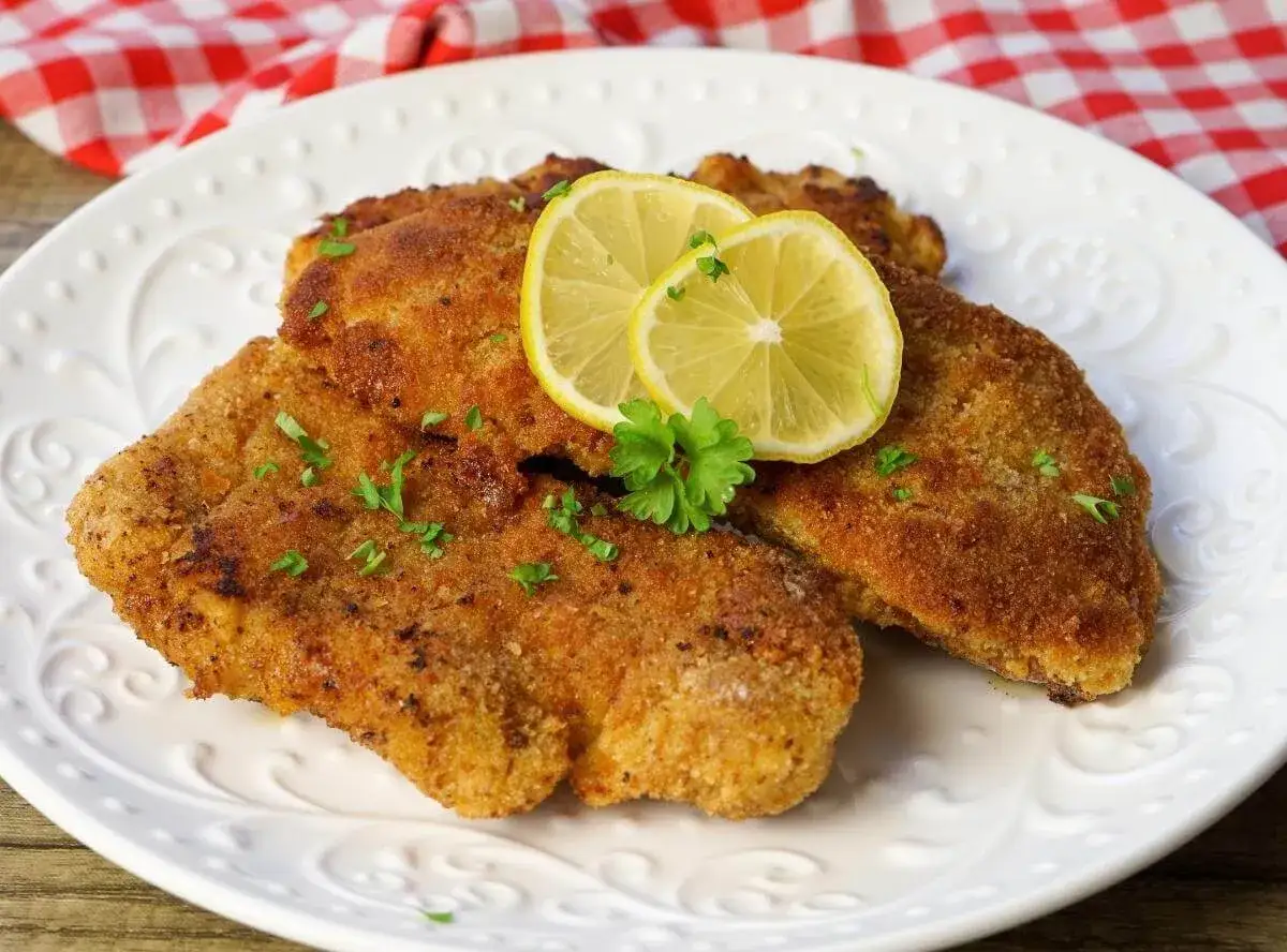 Drei goldbraune Schnitzel, perfekt paniert, liegen auf einem Teller. Zitronenscheiben und Petersilie garnieren das Gericht.