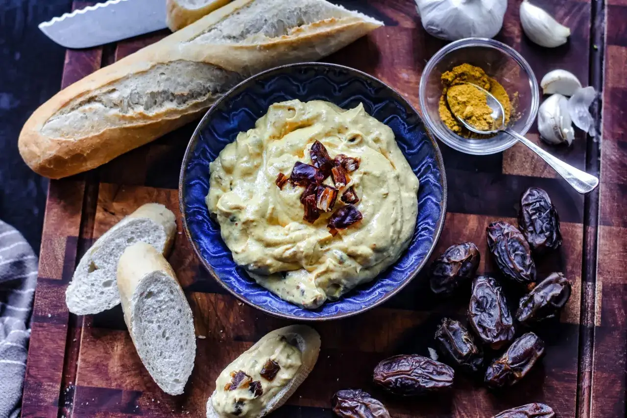 Cremiger Dattel Dip mit Baguettescheiben, Datteln, Knoblauch und Currypulver auf einem Holzbrett.