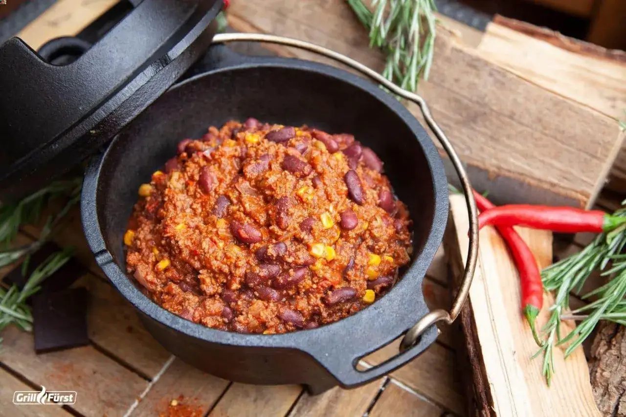 Herzhaftes Chili con Carne mit Kidneybohnen und Mais, serviert im Gusseisentopf, garniert mit frischem Rosmarin und roten Chilis.