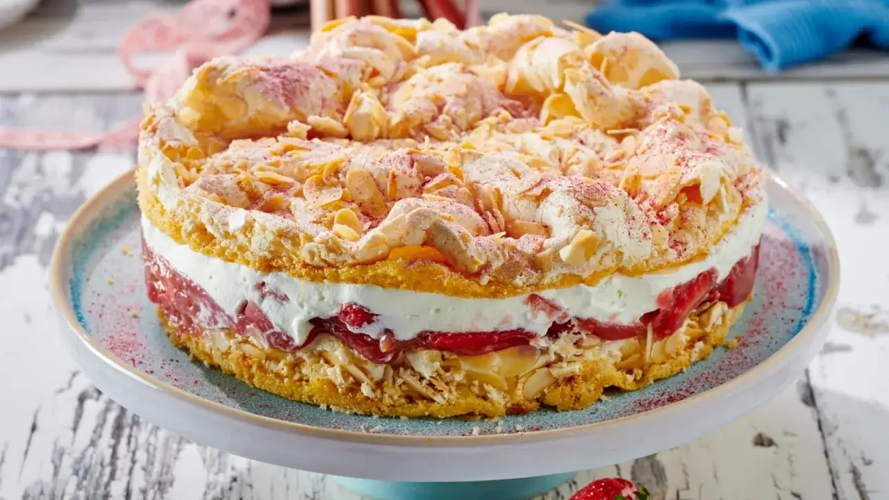 Ein k&ouml;stlicher Rhabarber Baiser Kuchen mit Biskuitb&ouml;den, Sahne und Rhabarberf&uuml;llung, garniert mit Mandelbl&auml;ttchen und Puderzucker.