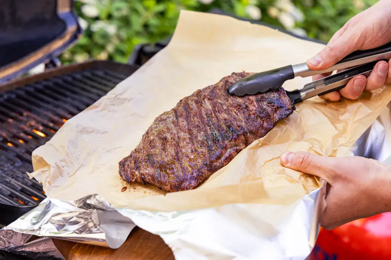 Frisch gegrilltes Flank Steak wird mit einer Zange auf Backpapier gehoben. Perfekt f&uuml;r den Sommer!