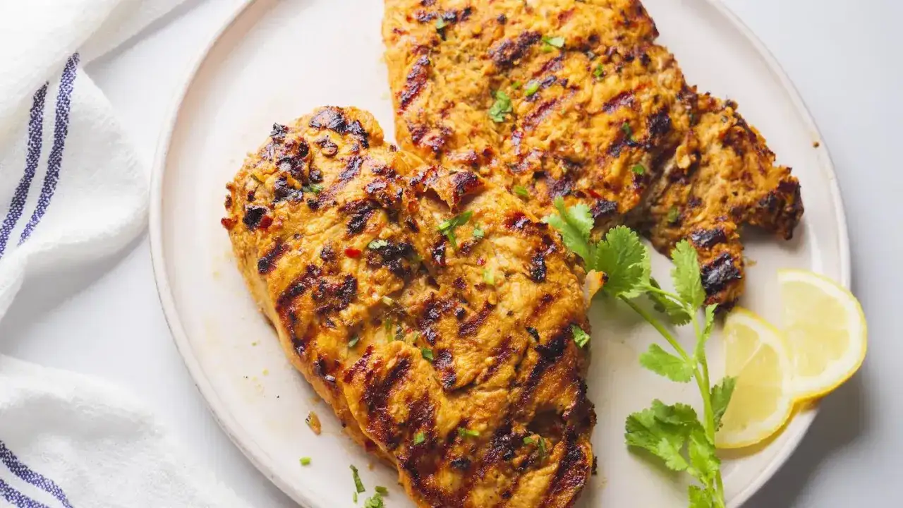 Zwei saftige Hähnchenbrustfilets, perfekt gegrillt mit markanten Streifen. Das Peri Peri Chicken ist mit Kräutern und Zitronenspalten garniert.
