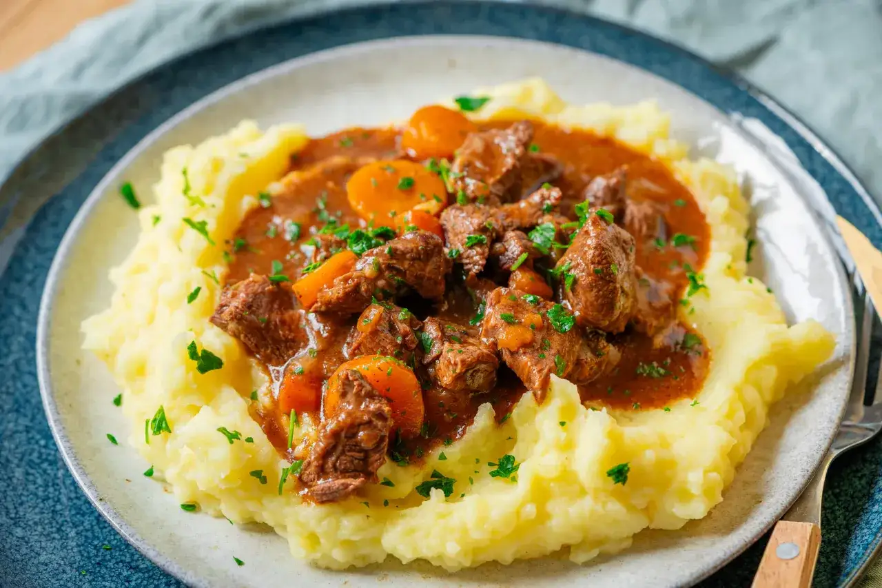 Boeuf Bourguignon, ein herzhafter Rindfleischeintopf mit Karotten in einer reichhaltigen Sauce, serviert auf cremigem Kartoffelp&uuml;ree und garniert mit Petersilie.