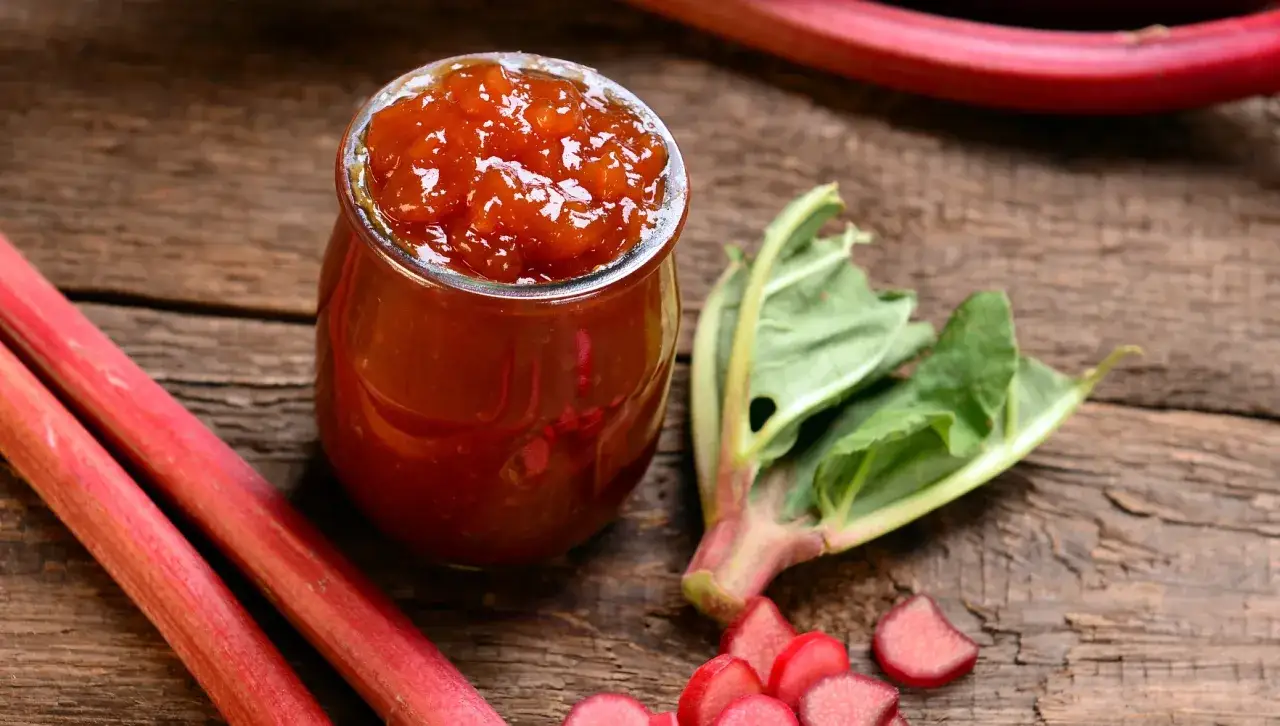 Rhabarbermarmelade im Glas, frische Stangen und Bl&auml;tter daneben. Perfekt, um Rhabarberschorle selber zu machen.