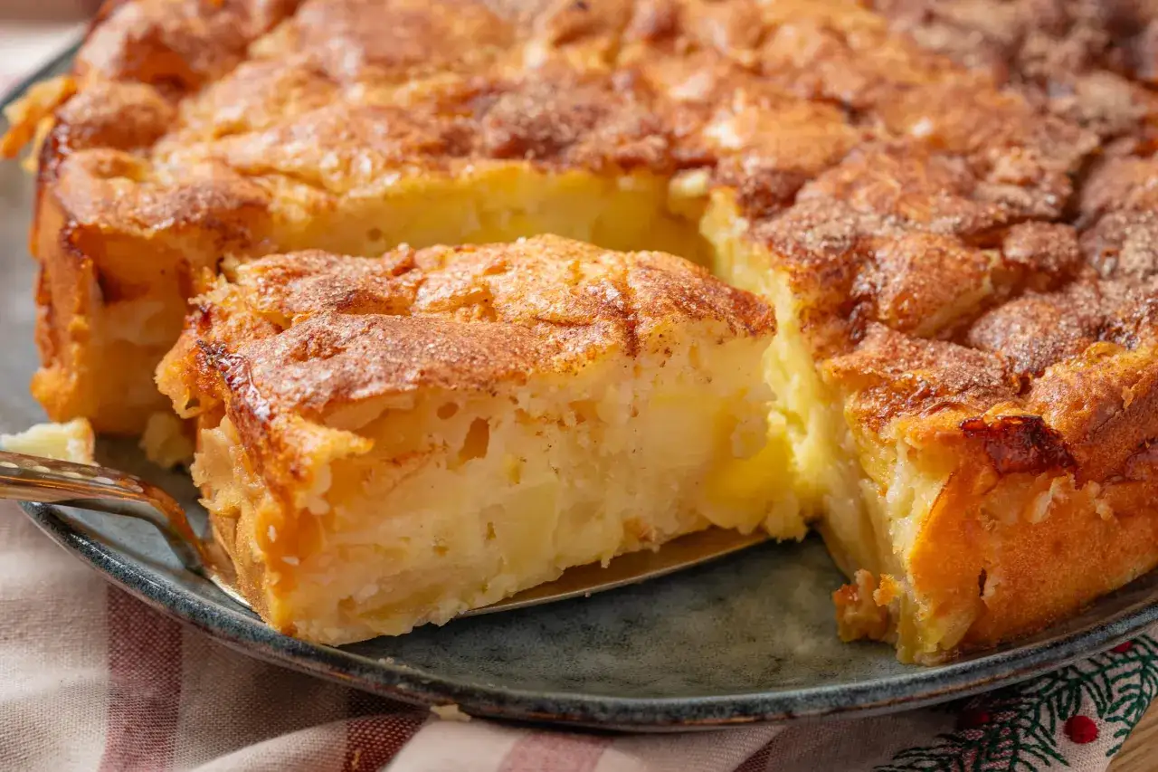 Ein saftiger apfelkuchen mit schale, goldbraun gebacken und mit Zimt bestreut. Ein St&uuml;ck wird gerade herausgehoben.
