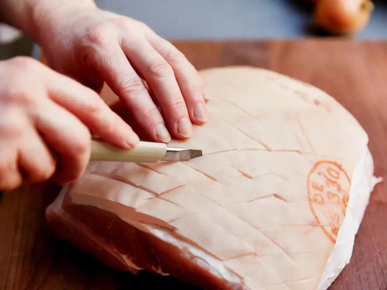 H&auml;nde ritzen die Schwarte eines Schweinebauchs ein, bereit f&uuml;r einen knusprigen Krustenbraten im Backofen.