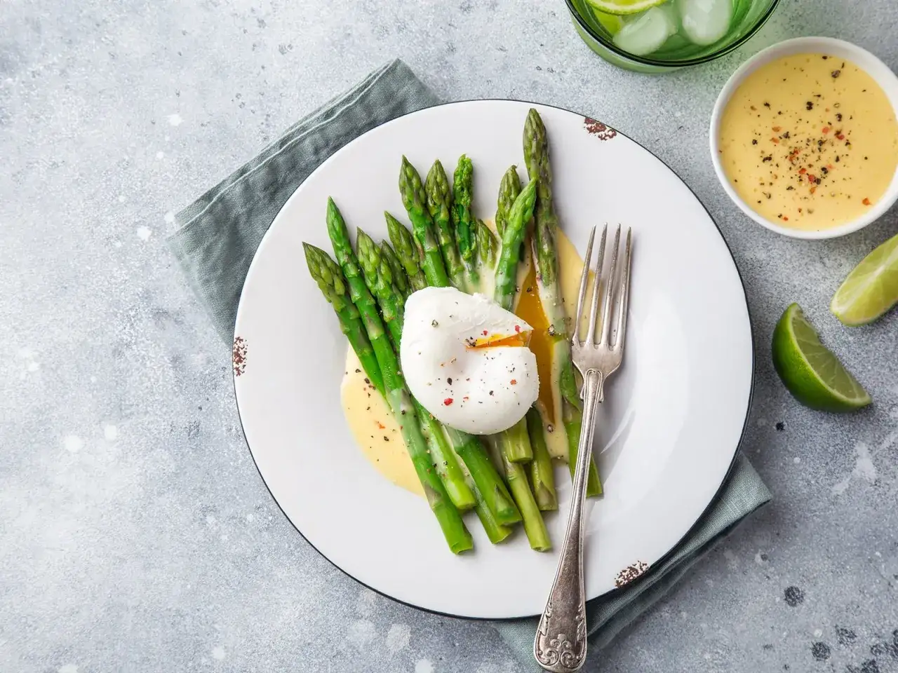 Spargel mit pochiertem Ei und cremiger sauce hollandaise, garniert mit Pfeffer und Limettenspalten.