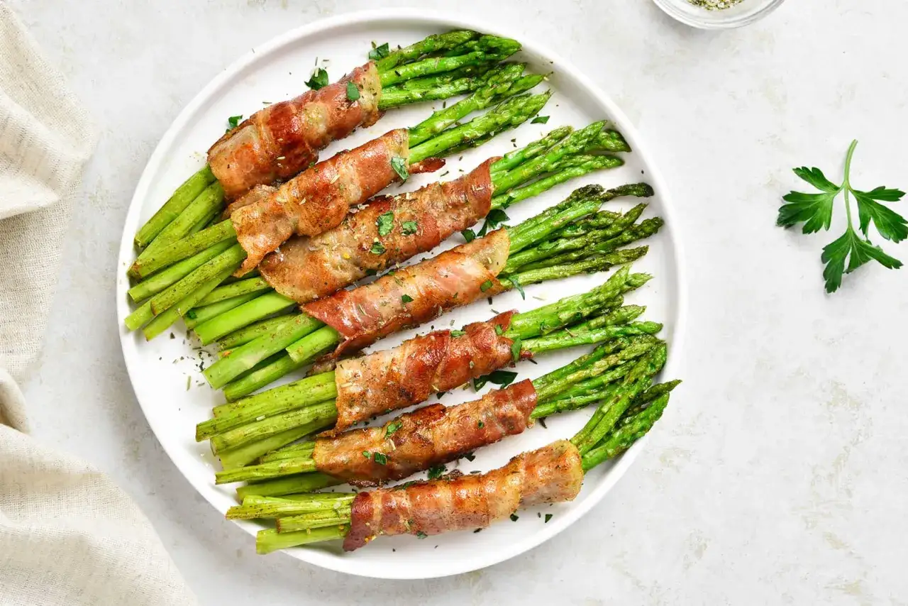 Saftige spargel im speckmantel, knusprig gebraten und mit Kr&auml;utern bestreut, auf einem wei&szlig;en Teller angerichtet.