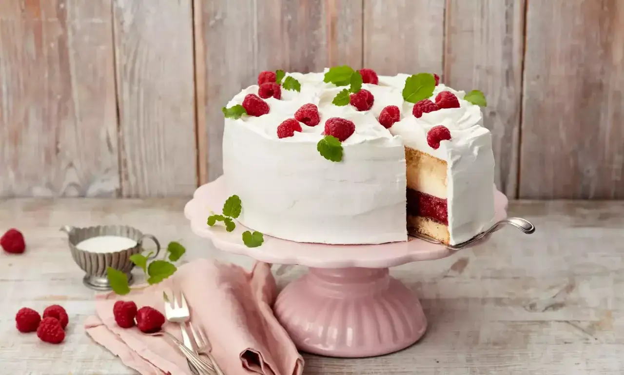 Himbeer Mascarpone Torte mit frischen Beeren und Minze, auf einem rosa Tortenst&auml;nder.