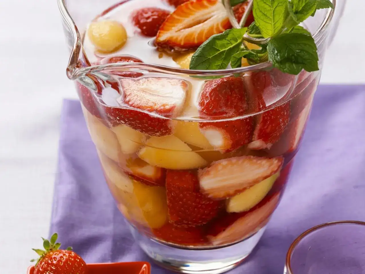 Erfrischende melonenbowle ohne alkohol, gef&uuml;llt mit Erdbeeren, Melonenb&auml;llchen und Pfirsichst&uuml;cken, garniert mit Minze.