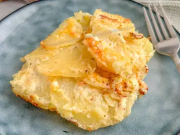 Ein Stück Kartoffelgratin einfach mit Sahne, goldbraun gebacken, auf einem blauen Teller. Daneben eine Gabel.
