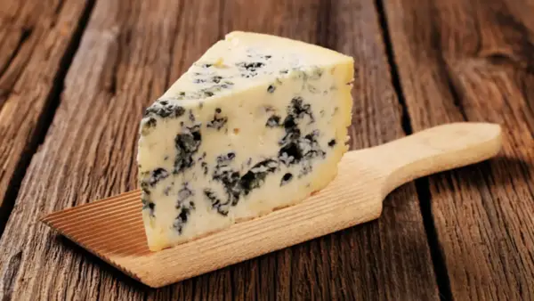 Ein Stück Blauschimmelkäse, perfekt für eine cremige blue cheese sauce, liegt auf einem Holzbrett.