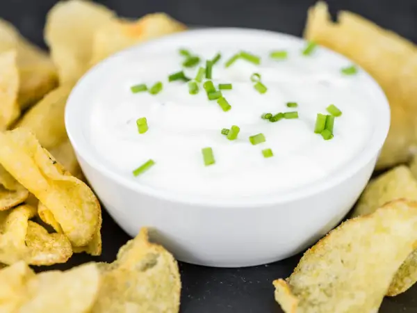 Schüssel mit cremiger Sour Cream, garniert mit Schnittlauch, umgeben von knusprigen Kartoffelchips.