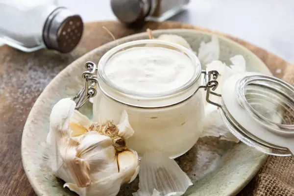 Frische Knoblauchsauce selber machen: cremige Sauce im Glas mit Knoblauchzehen und Salzstreuer im Hintergrund.