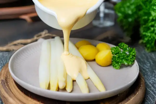 Sauce Hollandaise wird über weißen Spargel und Kartoffeln gegossen, um das Gericht zu verfeinern.