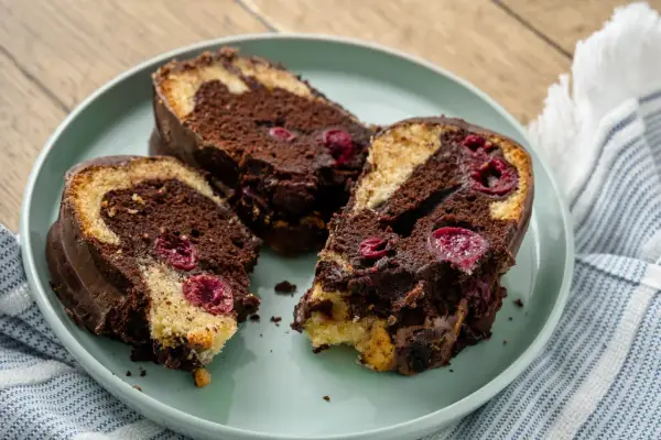 Drei saftige Stücke Marmorkuchen mit Kirschen und Schokoladenglasur auf einem Teller.