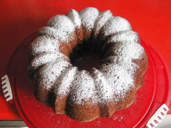 Omas Nusskuchen Gugelhupf, mit Puderzucker bestäubt, auf einem roten Teller.