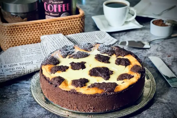 Ein köstlicher russischer Zupfkuchen mit Schokoladenboden und cremiger Füllung, bestäubt mit Puderzucker. Daneben eine Tasse Kaffee.