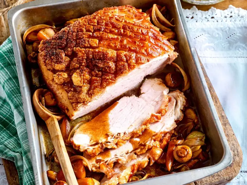 Saftiger Krustenbraten im Backofen, goldbraun und knusprig, mit Zwiebeln und Pilzen im Bratensaft. Ein Festmahl!