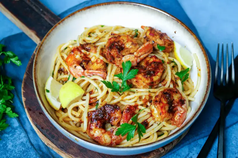 Ein Teller mit köstlichen Spaghetti mit Garnelen, garniert mit frischer Petersilie und Zitronenspalten.