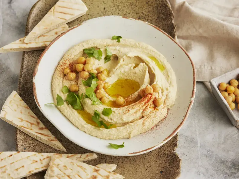 Cremiger Hummus, garniert mit Kichererbsen, Petersilie und Paprikapulver, serviert mit Pitabrot. Ein einfaches Hummus Rezept für Genießer.