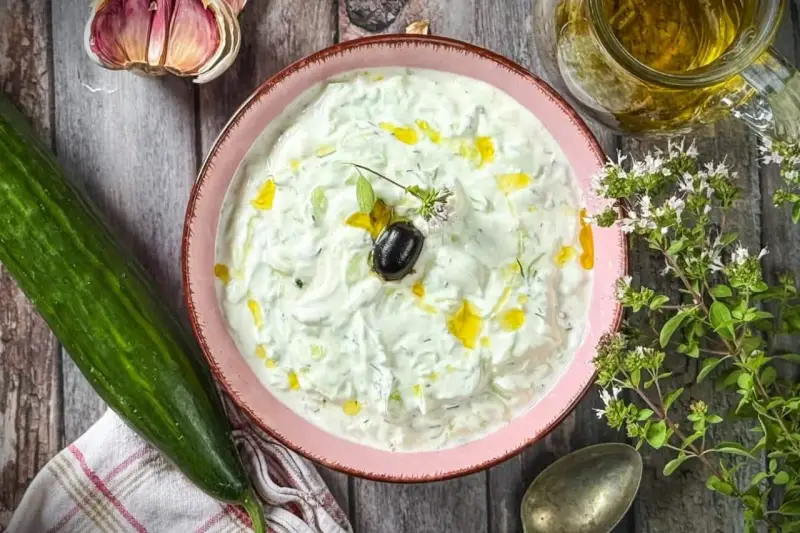 Frischer Tzatziki selbst machen: Cremiger Joghurt mit Gurke, Knoblauch, Dill und Olivenöl. Dazu eine Olive und Kräuter.