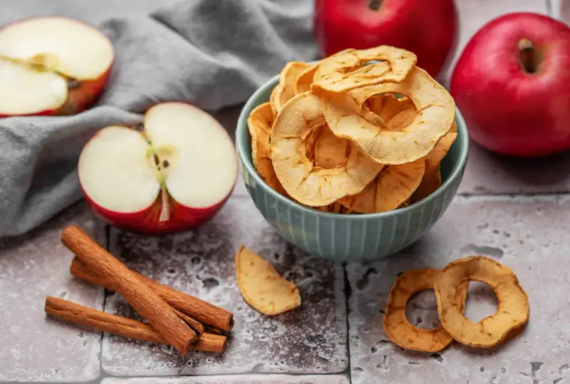 Leckere Apfelchips, die man ganz einfach selber machen kann, in einer Schüssel mit frischen Äpfeln und Zimtstangen.
